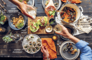 Top-down view of a seafood-based meal spread with hands hands actively cheers-ing